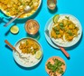 Two plates of fish curry alongside a pan with rice and lime wedges
