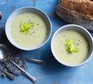 Celery soup in bowl topped with celery leaves, with spoons and bread