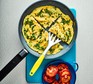 Omelette cut into quarters in pan with spatula and tomatoes