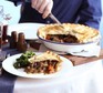 Steak, ale & mushroom pie in a round pie dish with slice out on a plate