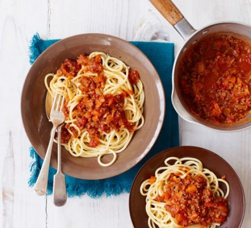 spaghetti bolognese on two plates, with sauce in a pan