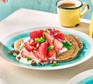 A serving of vegan strawberry pancakes on a plate with a cup of tea/coffee in the background
